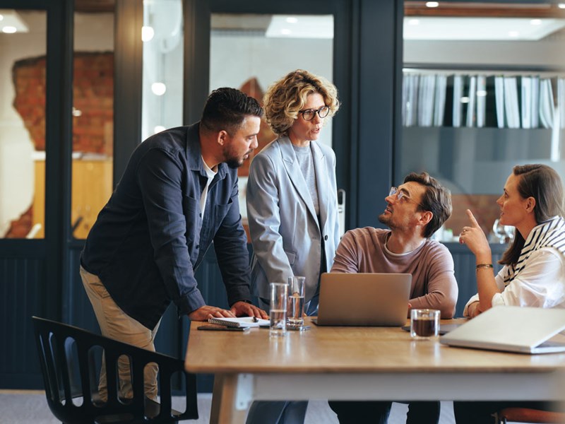 A group of coworkers talking at a desk in the office.